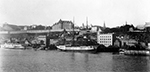 Photo en noir et blanc de la ville de Québec vue depuis un bateau à vapeur, avec des bateaux dans l'eau.