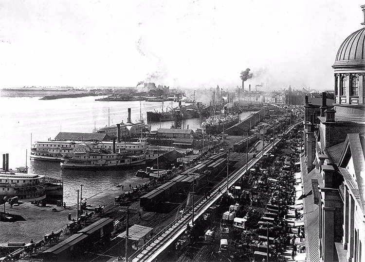 Photo en noir et blanc du port de Montréal vers 1900, prise depuis la chapelle Notre-Dame-de-Bon-Secours, montrant des bateaux et des voitures.