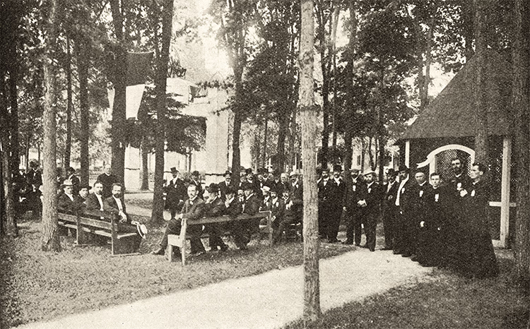 Photo ancienne d'un groupe d'hommes en costumes devant une église, lors des fêtes du conventum du Collège de Saint-Césaire en 1904.