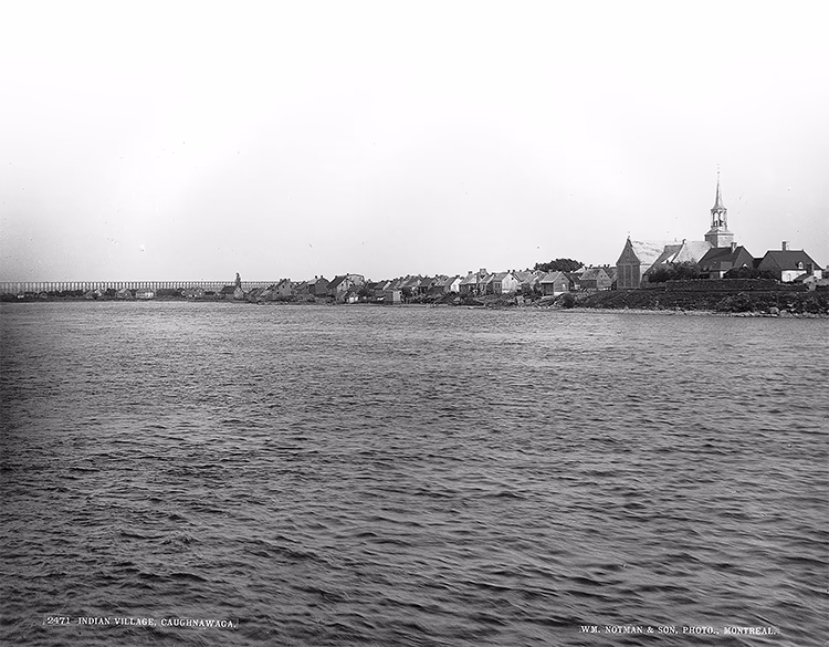 Photo en noir et blanc de Caughnawaga depuis le fleuve Saint-Laurent, vers 1885, montrant une ville au bord de l'eau.