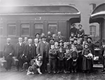 Photo en noir et blanc d’un groupe de personnes, des adultes, des enfants et un chien, posant devant un wagon de train en 1904.