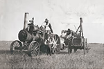 Photo en noir et blanc représentant une grosse machine agricole et trois hommes en habits propres.