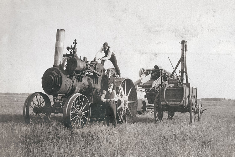 Photo en noir et blanc représentant une grosse machine agricole et trois hommes en habits propres.