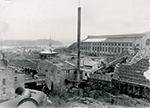 Vue en noir et blanc de la pulperie de Chicoutimi en 1918, avec bâtiments industriels en pierre et en brique, grandes fenêtres, cheminées et collines en arrière-plan.