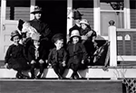 Portrait familial pris en 1919 montrant plusieurs enfants et deux adultes assis sur les marches d’un porche, vêtus de vêtements d’époque, avec chapeaux et manteaux.