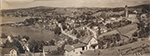 Vue panoramique de la ville de Newport en 1909, montrant un paysage vallonné avec le lac en arrière-plan, des maisons dispersées, des rues sinueuses et l’église Sainte-Marie avec son clocher dominant la scène. L’ensemble reflète un cadre rural et urbain typique du début du XXe siècle.