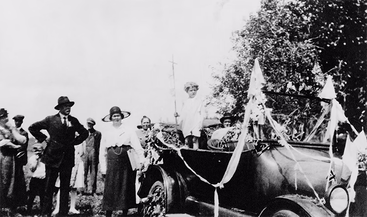 Photo en noir et blanc de personnes dans une vieille voiture lors de la fête de la Saint-Jean-Baptiste vers 1920.