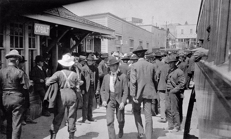 Photo en noir et blanc d’un groupe d'hommes se tenant devant une gare de Cobalt en Ontario, en 1906.