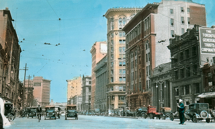 Photo ancienne, colorisée, de Main Street, à Winnipeg vers 1928, avec des piétons et des voitures circulant.