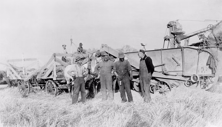 Un groupe d'hommes se tient devant une moissonneuse à la ferme de Joseph Begrand en 1923, avec Henri Begrand au centre.